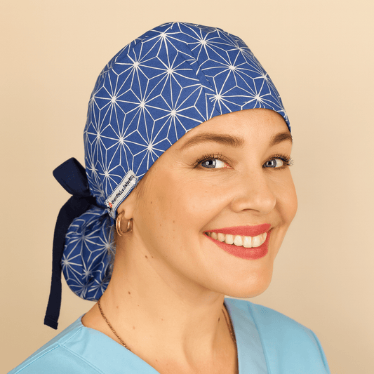Blue scrub cap with geometric star pattern, tie back style, and Everyday Heroes label. Modeled by a smiling woman in a light blue scrub top with gold hoop earrings, this surgical hat is ideal for nurses, doctors, and surgeons. Comfortable ponytail scrub cap, reusable and washable, perfect for medical, dental, or hospital staff.