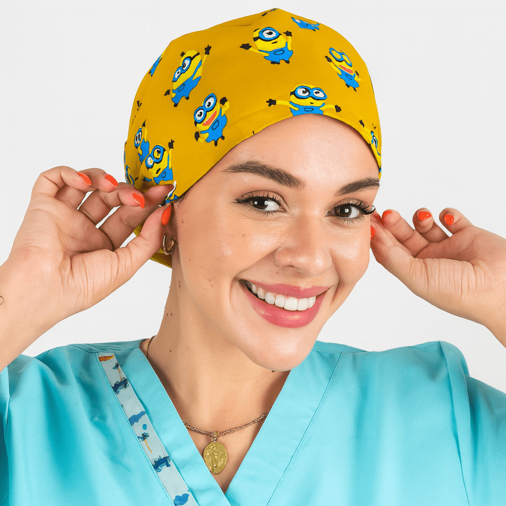 Smiling woman wearing a yellow euro scrub cap with blue cartoon character print. Fun pediatric scrub hat with satin lining, customizable with name embroidery. Ideal for nurses, surgeons, and OR professionals looking for playful comfort.
