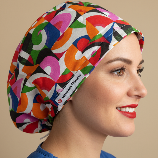 Woman wearing colorful abstract geometric scrub cap in profile view - vibrant pink, orange, red, green, blue curved shapes on white background - euro style surgical hat with satin lining and everydayheroescaps label - professional medical headwear for nurses and doctors