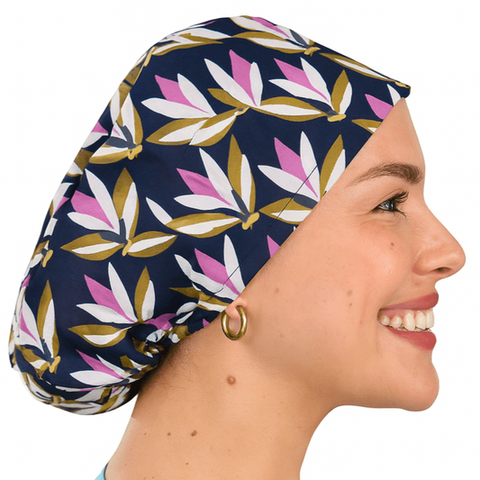 Smiling woman wearing a navy floral euro scrub cap with pink and olive leaf print. Custom satin-lined surgical hat for nurses, surgeons, and estheticians. Lightweight, stylish, and professional scrub cap providing comfort and hair protection during long shifts.