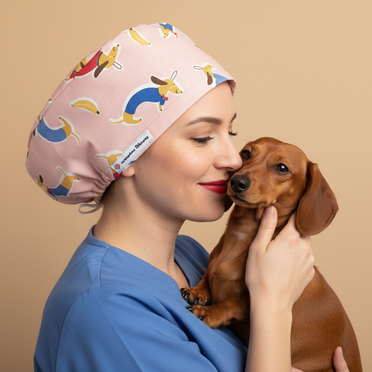 Veterinarian woman holding small dachshund dog with heads touching affectionately - wearing pink scrub cap with playful dachshund print pattern - euro style surgical hat with satin lining and everydayheroescaps label - professional medical headwear for vets and animal lovers