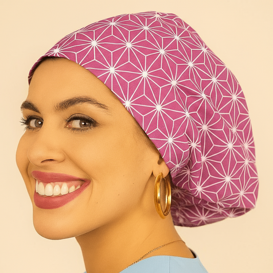 A woman with a pink geometric patterned cap and gold hoop earrings is smiling at the camera.