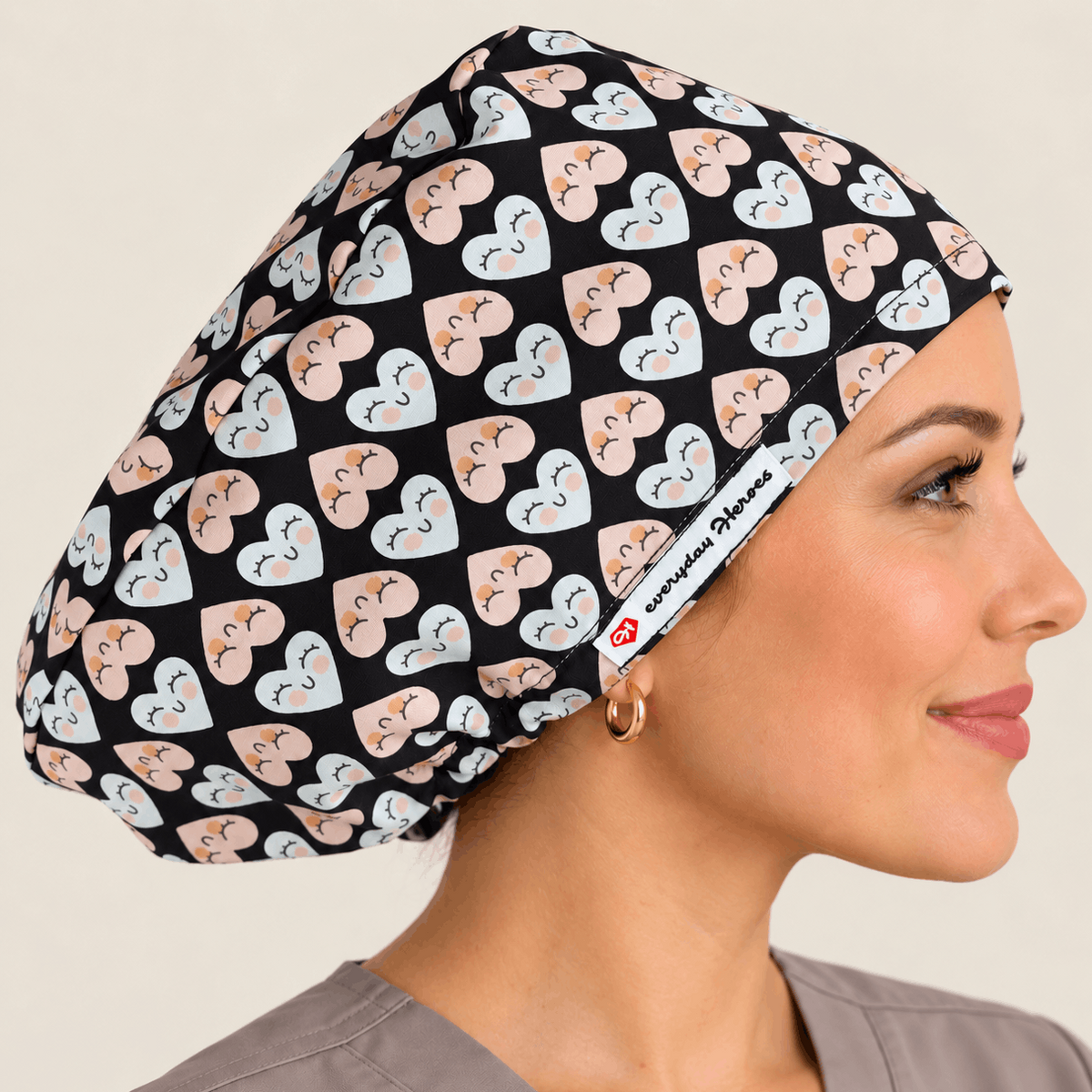 A woman in profile wearing a black scrub cap with a repeating pattern of light blue and peach hearts with small medical symbols. 