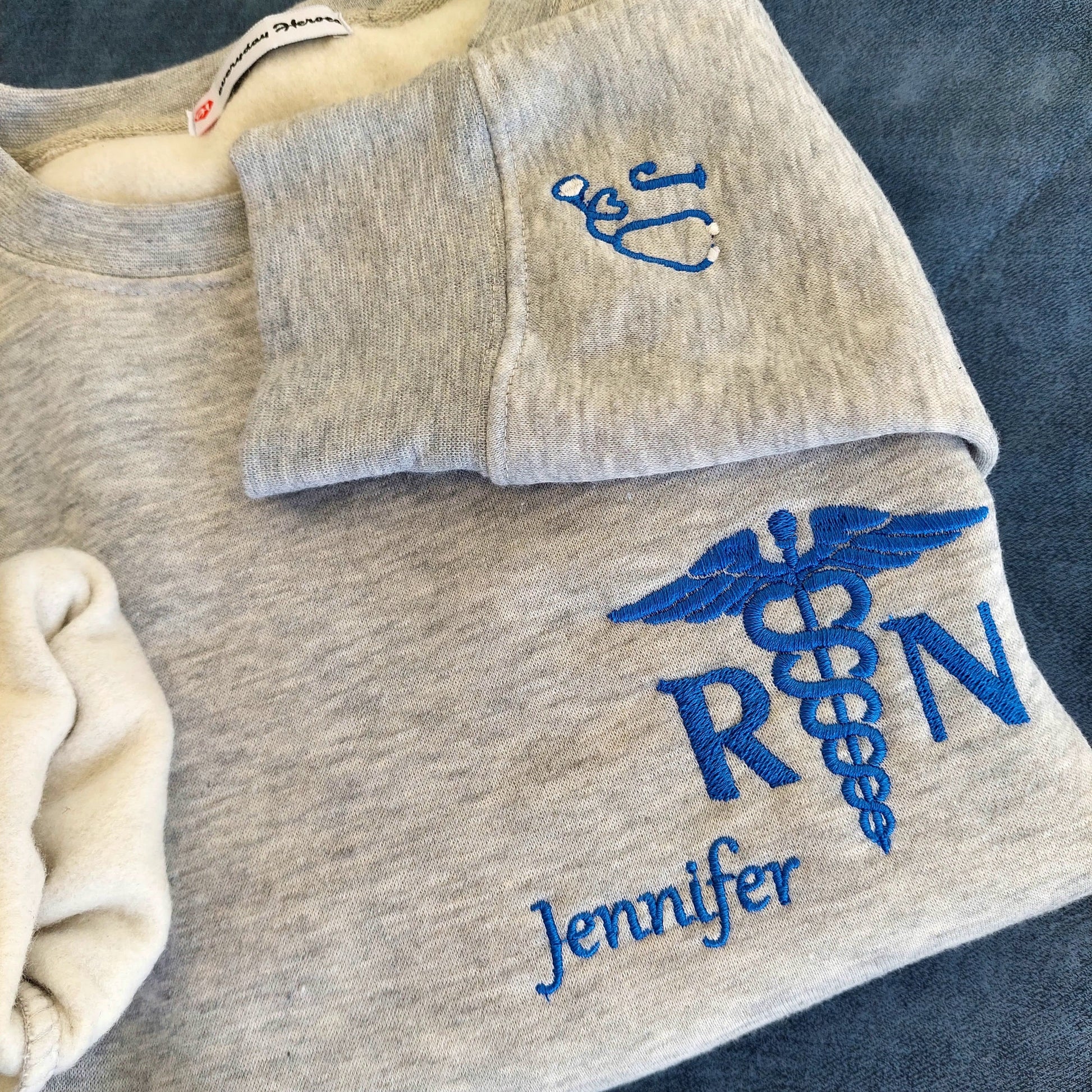 Crewneck Fleece Sweatshirt Personalized Nurse Name - [scrub_hat]-[scrub_capSample shown with Royal Blue thread for name and caduceus & credentials on grey melange sweatshirt*_for_women]-[surgical_cap]
