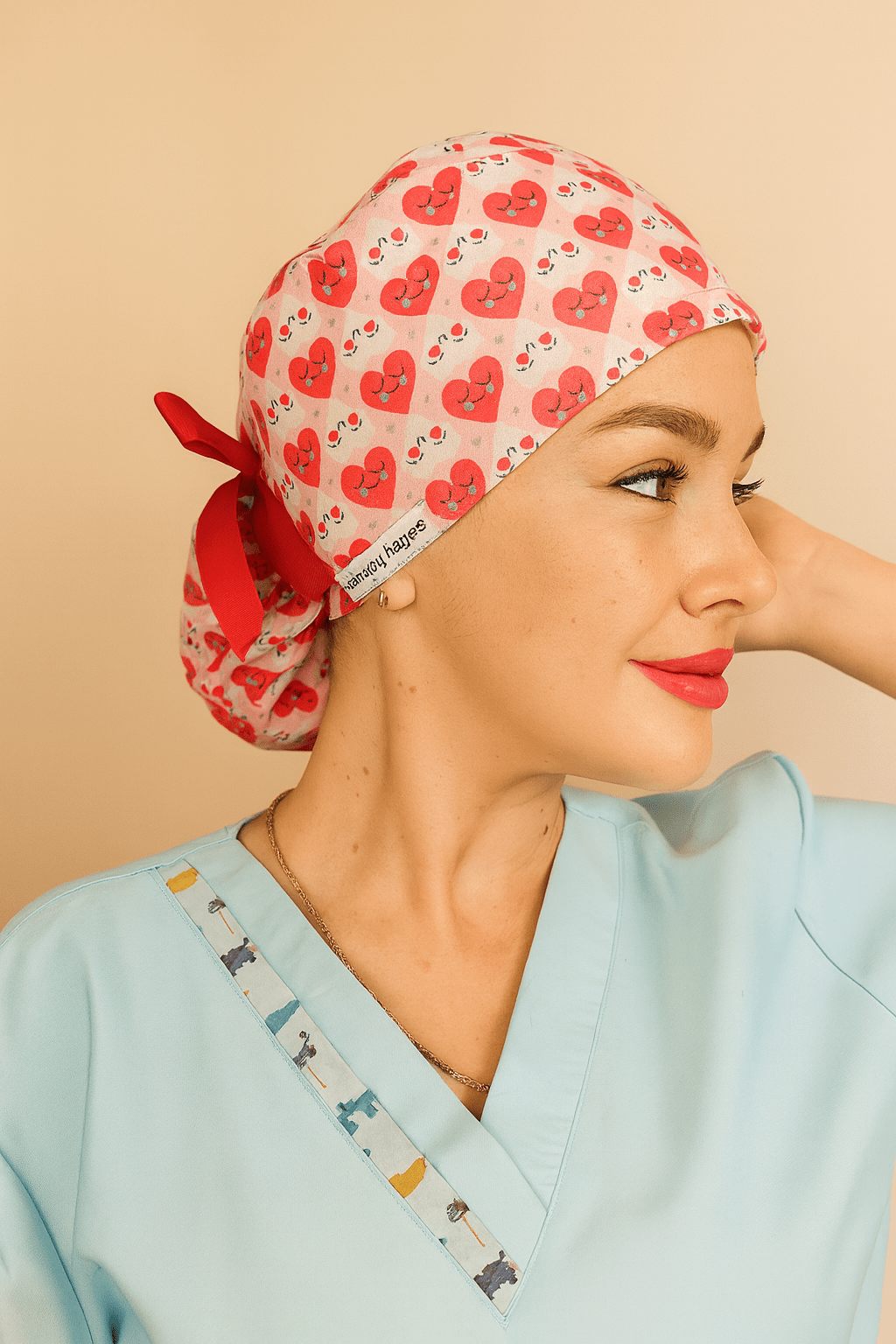Smiling woman wearing a vibrant scrub cap covered in red and pink heart designs with cute smiley faces. The cap features a red ribbon tied at the back and a visible label reading "everyday beauty." Ideal for healthcare professionals, nurses, and doctors seeking stylish, comfortable, and expressive scrub caps. Photo showcases cheerful personality and premium stitching detail, perfect for Valentine’s Day or themed workwear.