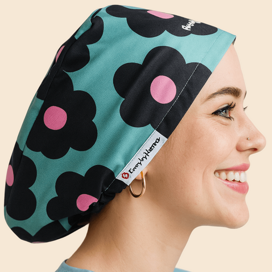 A woman wearing a blue shirt and a black and pink floral cap with a pink dot on it, smiling at the camera.