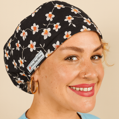 A woman wearing a black and white floral patterned cap and a light blue shirt is smiling at the camera.