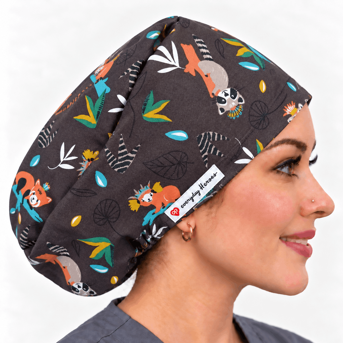 A woman in profile wearing a dark gray scrub cap with a colorful cartoon animal and leaf print. .