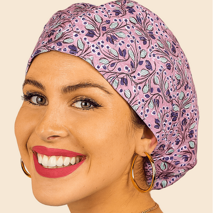 A woman with a purple and blue patterned hair cap and large hoop earrings is smiling at the camera.