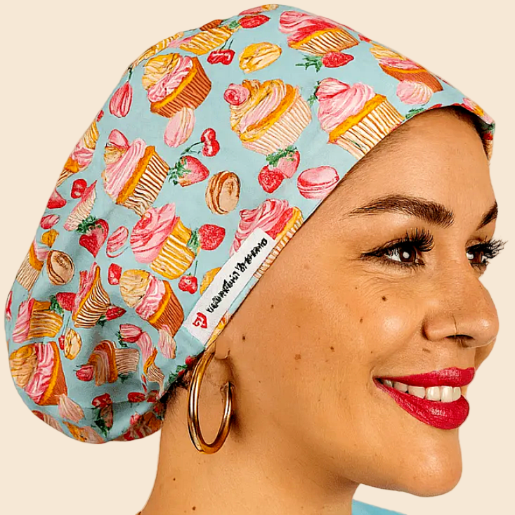 A woman wearing a blue cap with a pattern of cupcakes and strawberries, smiling at the camera.