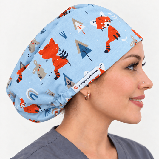 A woman in profile wearing a light blue scrub cap with a playful cartoon animal print of red foxes, rabbits, and trees. The scrubs cap features a white elastic band with the brand name 'everything medically' printed on it.