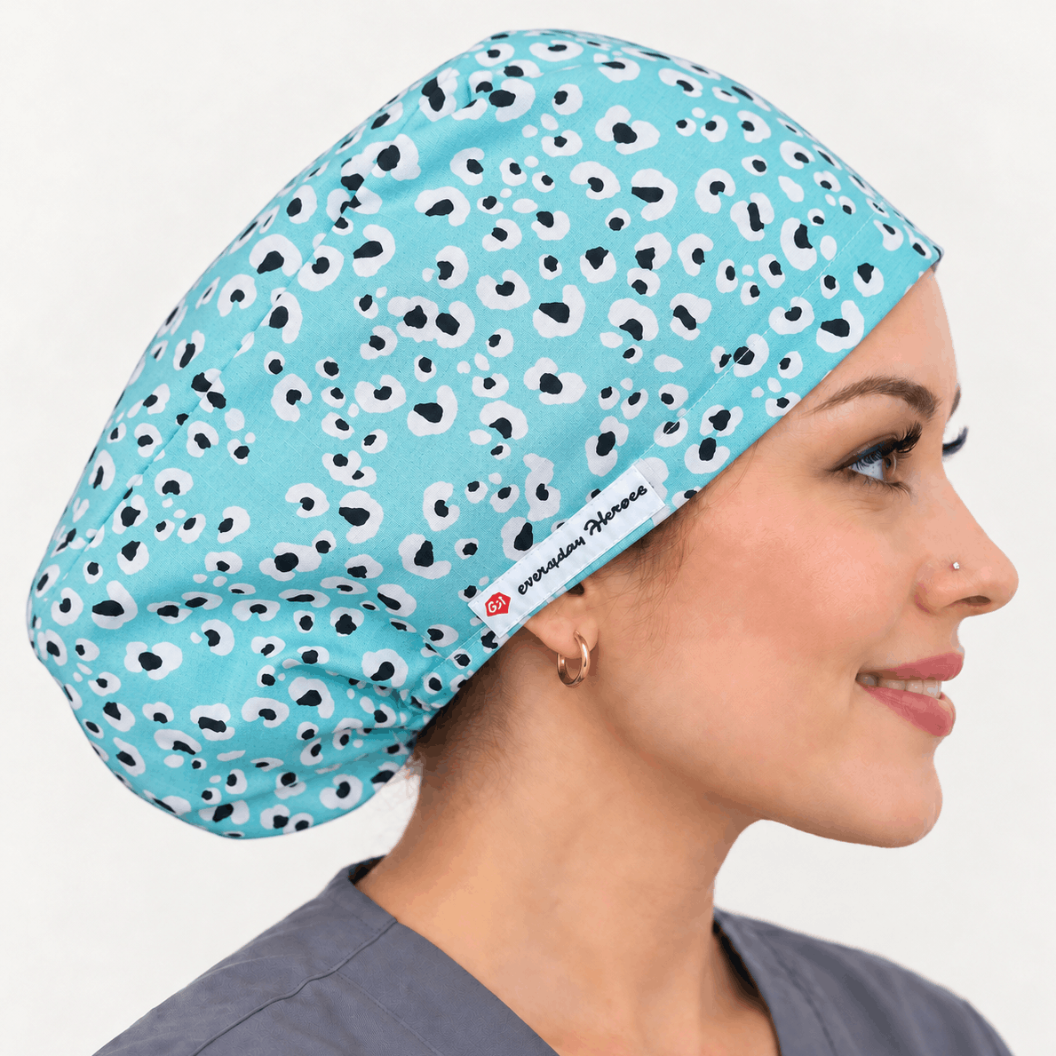 A woman in profile wearing a light blue scrub cap with a black and white spotted pattern. The brand name 'eMedica' is visible on a small white label near the edge of the cap.