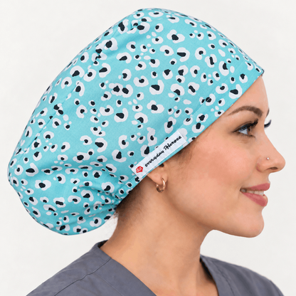 A woman in profile wearing a light blue scrub cap with a black and white spotted pattern. The brand name 'eMedica' is visible on a small white label near the edge of the cap.
