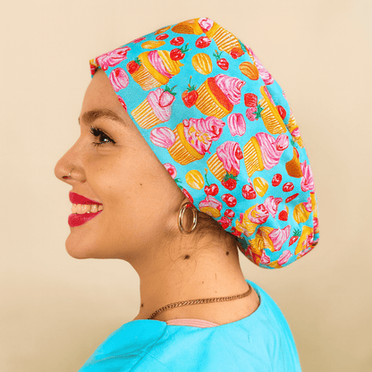 A woman wearing a blue cap with a pattern of cupcakes and strawberries smiling.