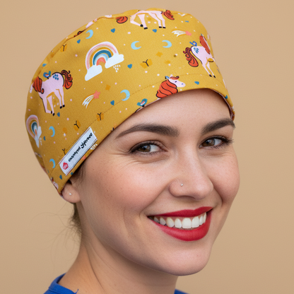 Beautiful woman in 3/4 angle wearing mustard yellow unicorn scrub cap - whimsical pattern with pink unicorns, rainbows, moons and stars - euro style bouffant surgical hat with puffy back and everydayheroescaps label - professional medical headwear for nurses and pediatric healthcare workers
