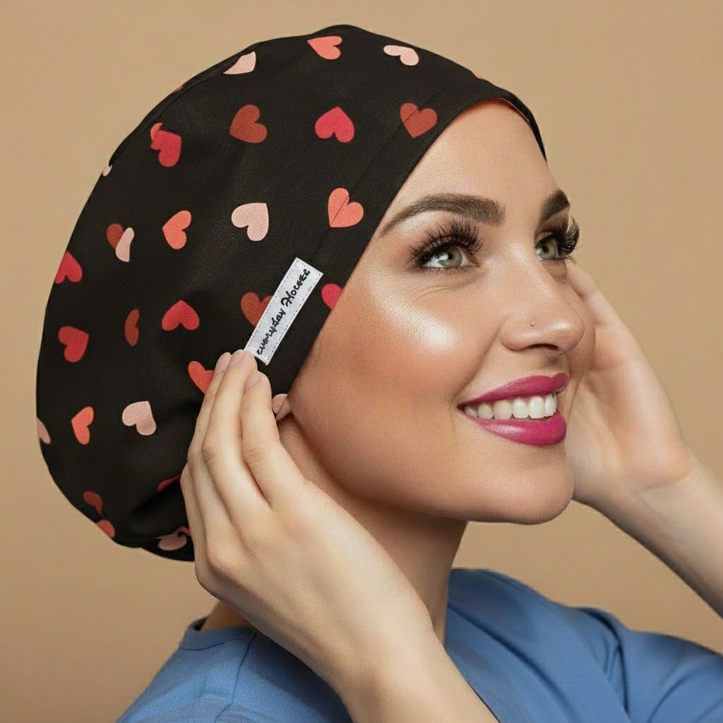 Black pink coral hearts scrub cap back side view with smiling healthcare professional - romantic scattered hearts pattern featuring pink coral and light pink hearts on black background - euro style bouffant surgical cap for women - custom satin lined with name embroidery option - adjustable elastic fit - woman with hot pink lipstick green hazel eyes showing confident smile - Everyday Heroes brand label visible - 