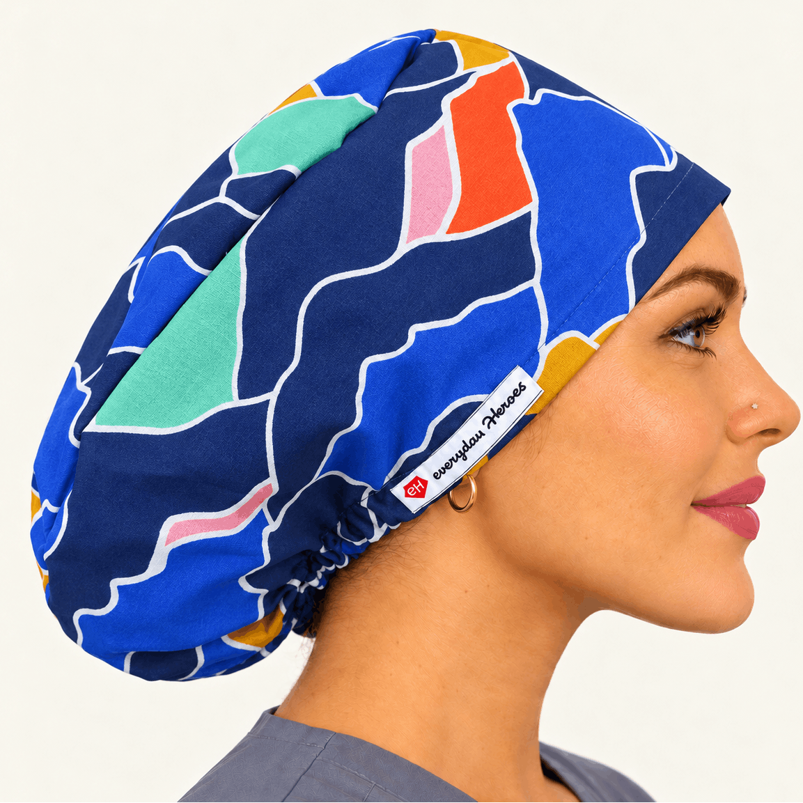 A woman in profile wearing a blue scrub cap with a colorful abstract geometric pattern in teal, orange, pink, and yellow.