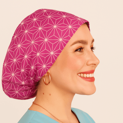 Smiling woman wearing a fuchsia Japanese Asanoha pattern euro scrub cap. Satin-lined and adjustable for comfort, this custom surgical hat is ideal for nurses, theatre staff, and medical professionals. Personalized with name embroidery for a unique touch.