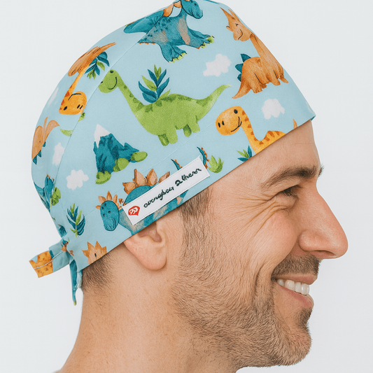 Smiling male doctor wearing a light blue scrub cap with colorful dinosaur prints. Comfortable and adjustable men’s surgeon hat designed for doctors, surgeons, and pediatric professionals. A fun and practical gift for doctors who bring joy to their patients.
