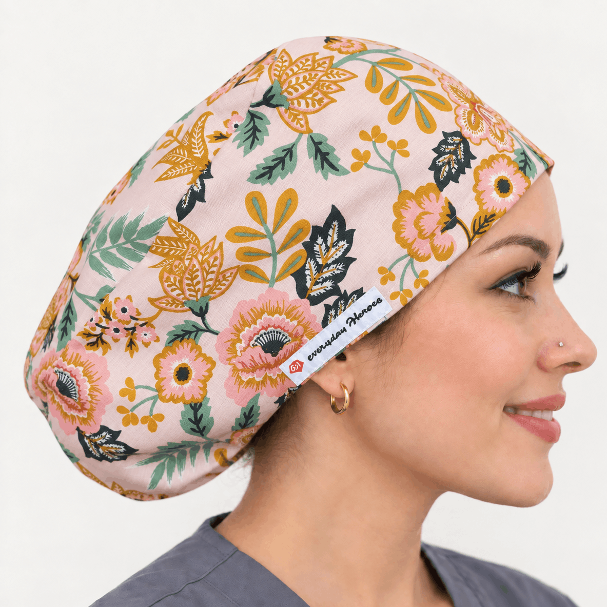 A woman in profile wearing a floral-patterned scrub cap. The cap has a light pink base with yellow, orange, green, and black botanical motifs.