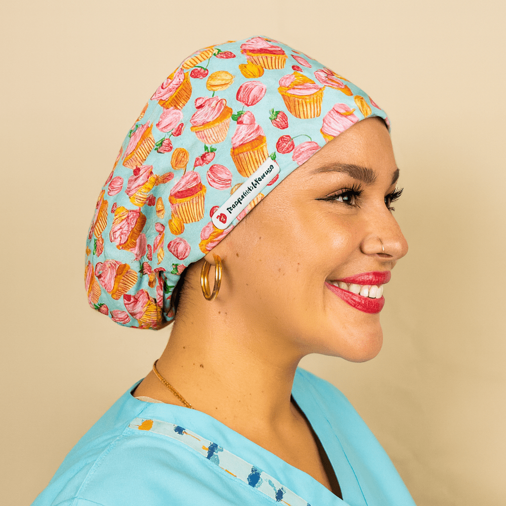 A woman wearing a blue scrubs cap with a pattern of cupcakes and strawberries, smiling at the camera.