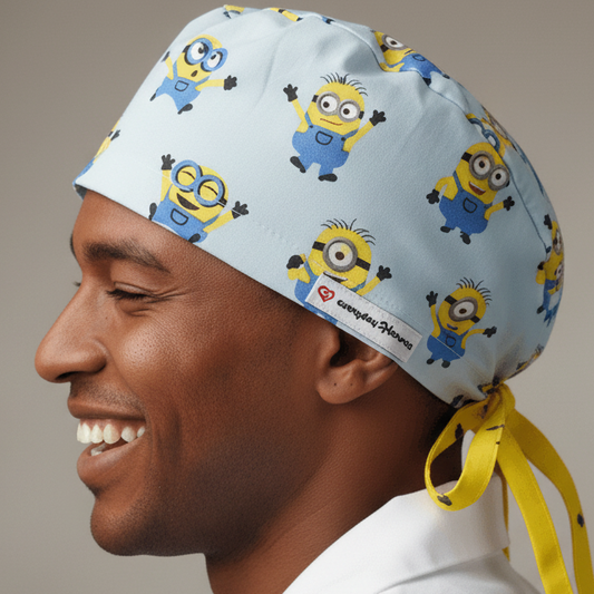 Funny Men's Surgeon Cap featuring Minions cartoon characters on light blue fabric. Comic Characters Custom Scrub Cap with Name personalization option, shown on white mannequin side view with Everyday Heroes label. Doctors Personalized Gift Surgical Cap With Name embroidery available. Adjustable bouffant euro style medical headwear for healthcare professionals. Minion scrub cap in blue 