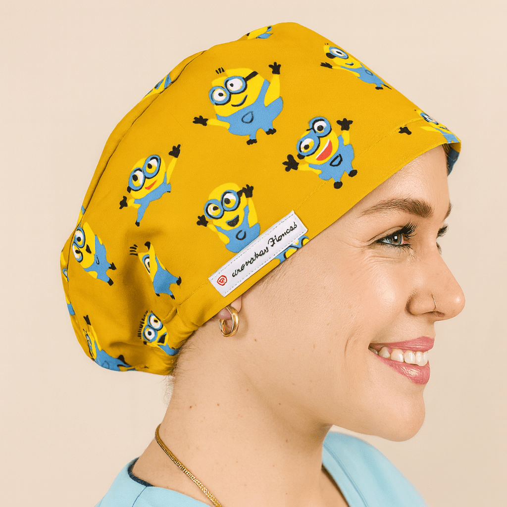 Smiling woman wearing a yellow euro scrub cap with blue cartoon character print. Fun pediatric scrub hat with satin lining, customizable with name embroidery. Ideal for nurses, surgeons, and OR professionals looking for playful comfort.