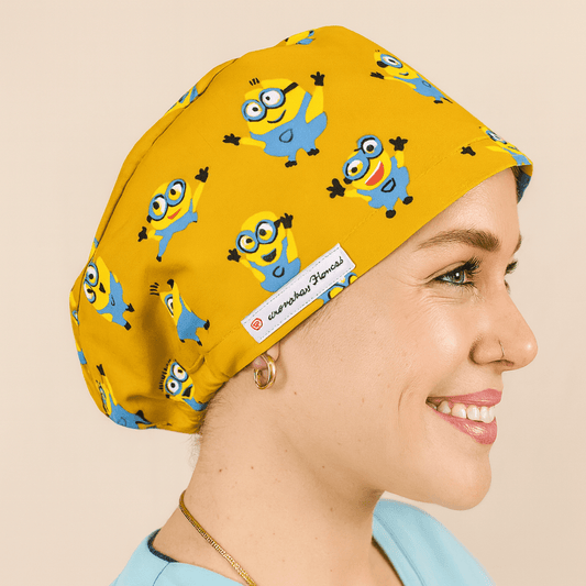 Smiling woman wearing a yellow euro scrub cap with blue cartoon character print. Fun pediatric scrub hat with satin lining, customizable with name embroidery. Ideal for nurses, surgeons, and OR professionals looking for playful comfort.