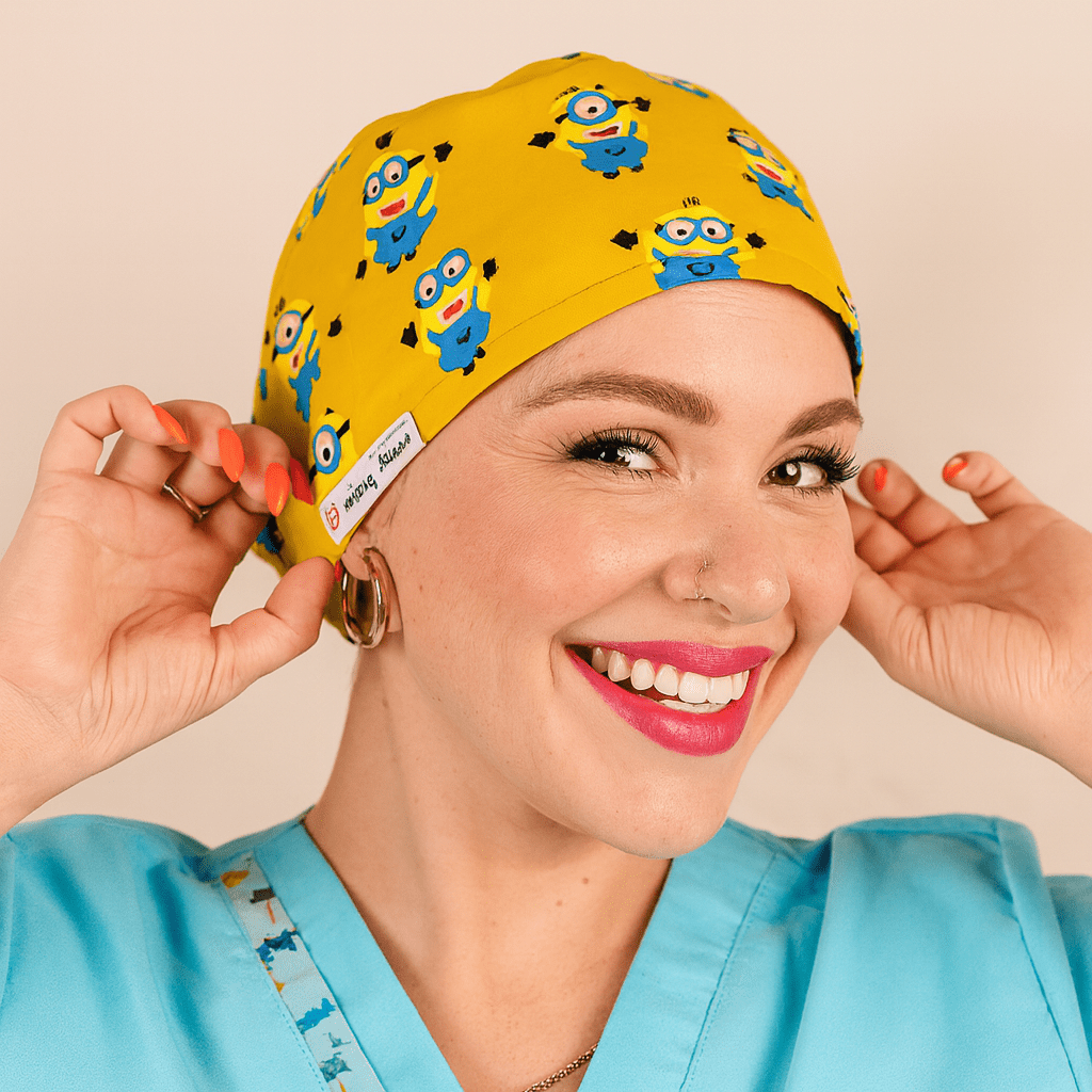 Smiling woman wearing a yellow euro scrub cap with blue cartoon character print. Fun pediatric scrub hat with satin lining, customizable with name embroidery. Ideal for nurses, surgeons, and OR professionals looking for playful comfort.