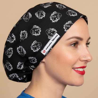Woman wearing black scrub cap with Einstein face pattern in profile view - euro style surgical hat with white sketched Einstein portraits on black fabric - satin lining and everydayheroescaps label - professional medical headwear for nurses, doctors and science lovers
