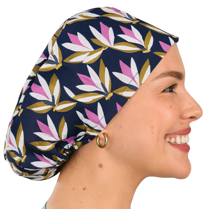 Smiling woman wearing a navy floral euro scrub cap with pink and olive leaf print. Custom satin-lined surgical hat for nurses, surgeons, and estheticians. Lightweight, stylish, and professional scrub cap providing comfort and hair protection during long shifts.