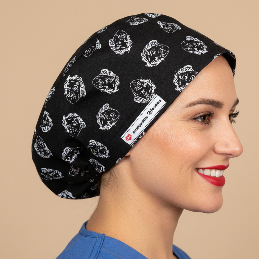 Woman wearing black scrub cap with Einstein face pattern in profile view - euro style surgical hat with white sketched Einstein portraits on black fabric - satin lining and everydayheroescaps label - professional medical headwear for nurses, doctors and science lovers
